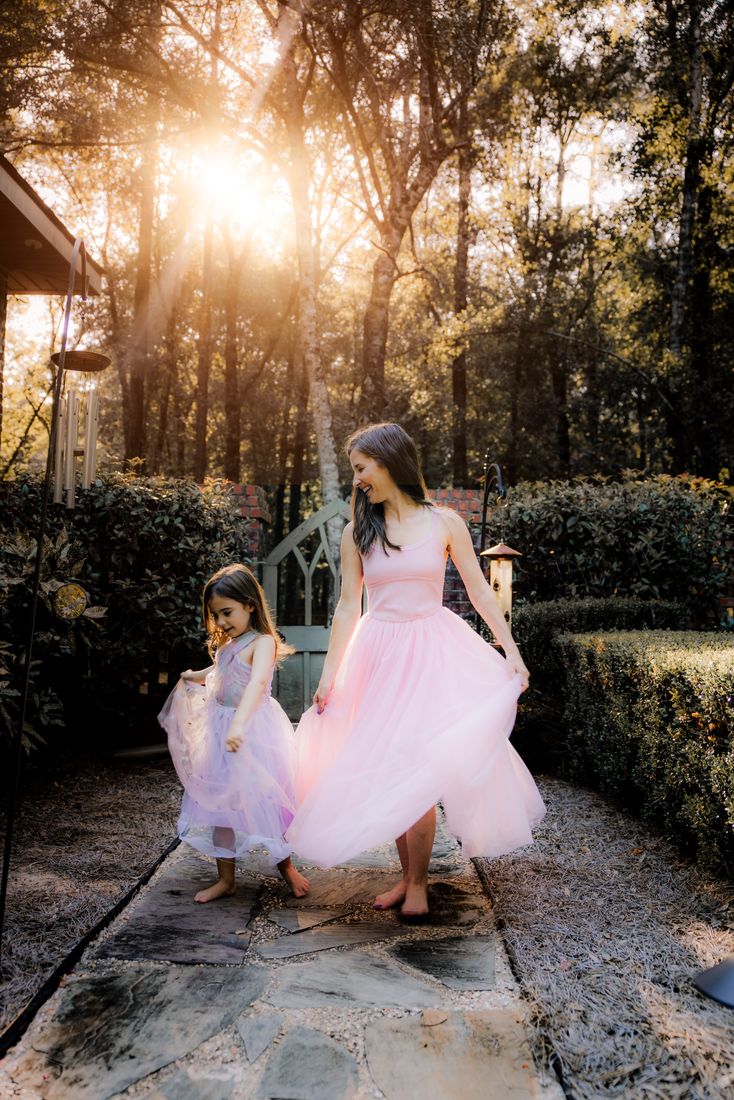 A mother and daughter in matching tulle dresses twirling on a garden path in the backlight