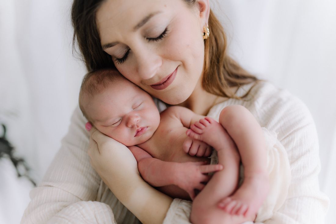 A mother with her eyes closed, resting her cheek against her sleeping newborn's head