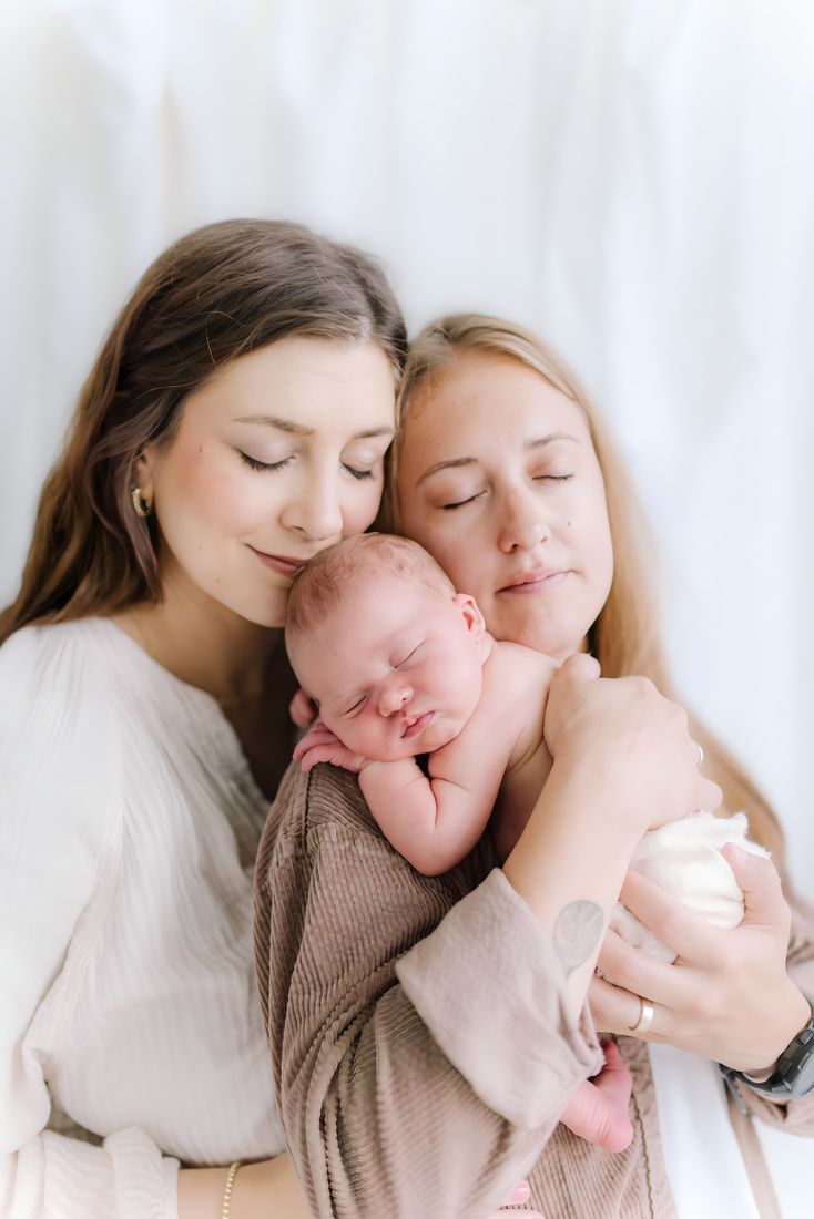 Two parents leaning together with their swaddled newborn asleep between them