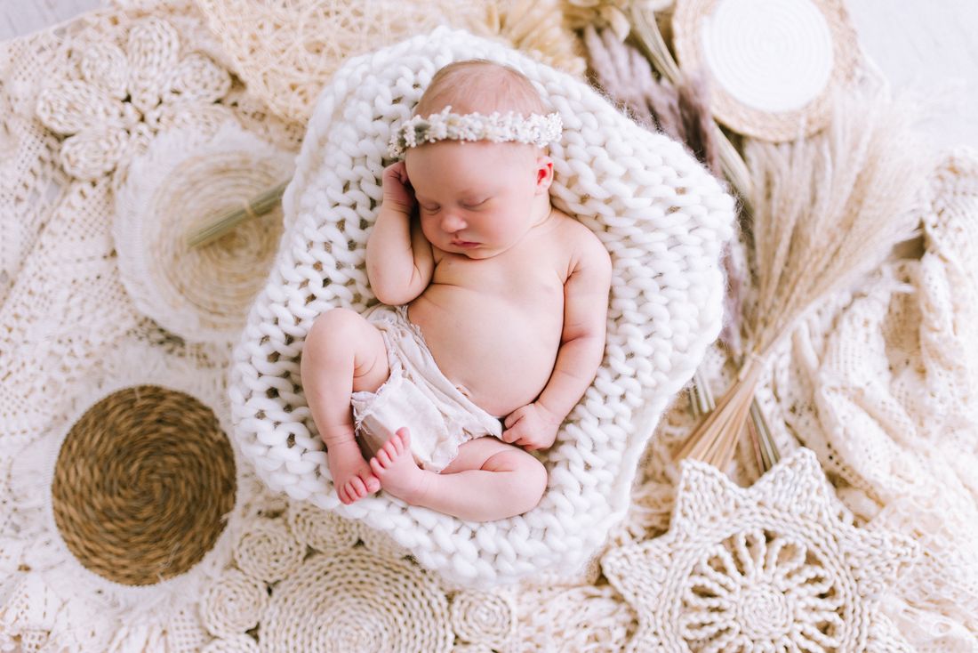 Overhead view of a newborn in a flower crown curled up on a chunky knit blanket