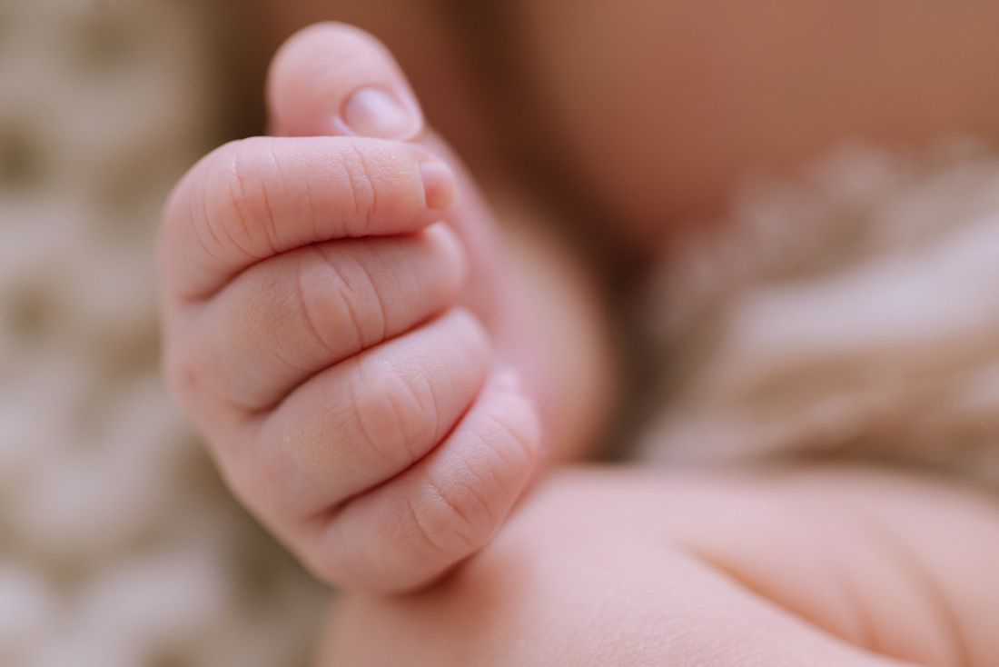 Close-up of a newborn's curled fist against a cream blanket